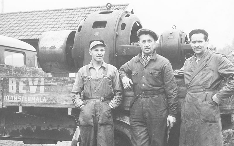 Tre män i arbetskläder vid en lastbil med en stor elmotor på flaket, omkring 1940.